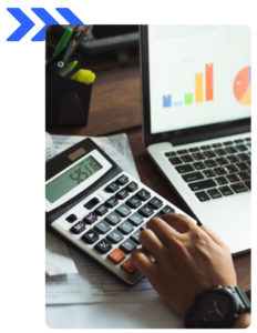 Close-up of hand using a calculator with a laptop displaying colorful bar and pie charts.