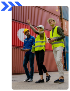 Three logistics workers in safety vests and helmets standing in front of shipping containers, discussing operations.